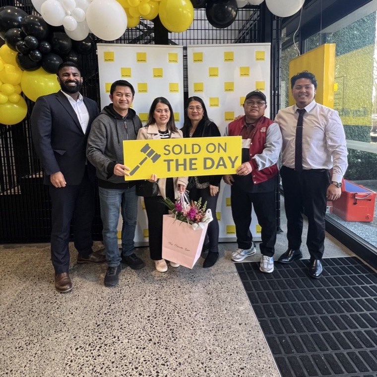 A family with their Sold on the Day sign at Ray White Manukau